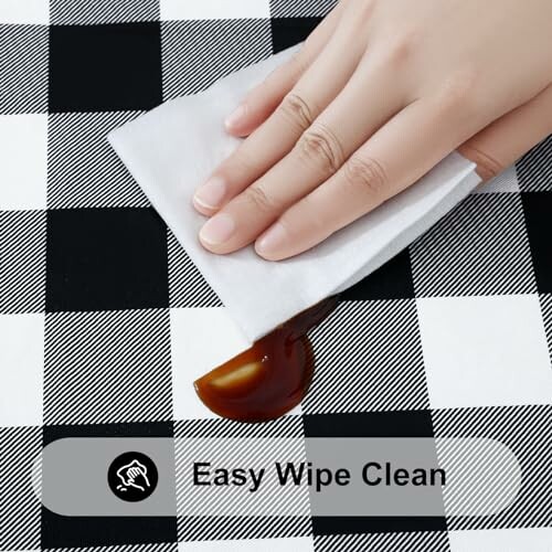 A hand wiping a spill on the black and white checkered tablecloth.