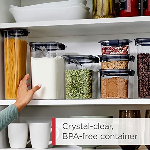 Hand reaching for BPA-free kitchen storage containers filled with pasta, flour, beans, and spices on a pantry shelf.