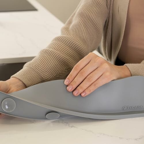 Person using a gray kitchen utensil on a counter.