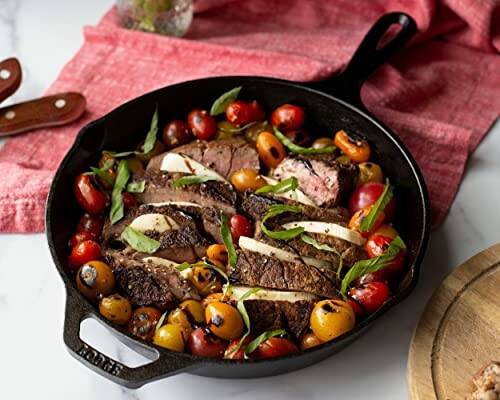 Sliced steak in cast iron skillet with tomatoes and basil.